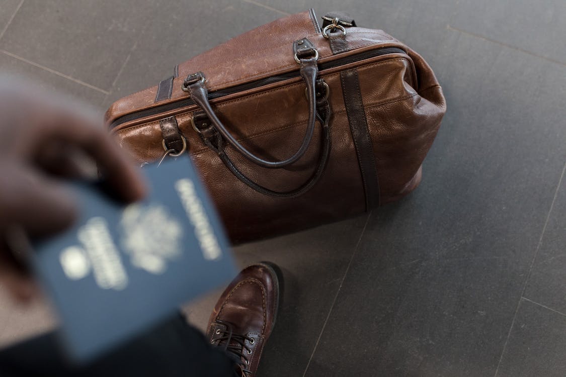 leather duffle bag on floor with man holding passport in foreground